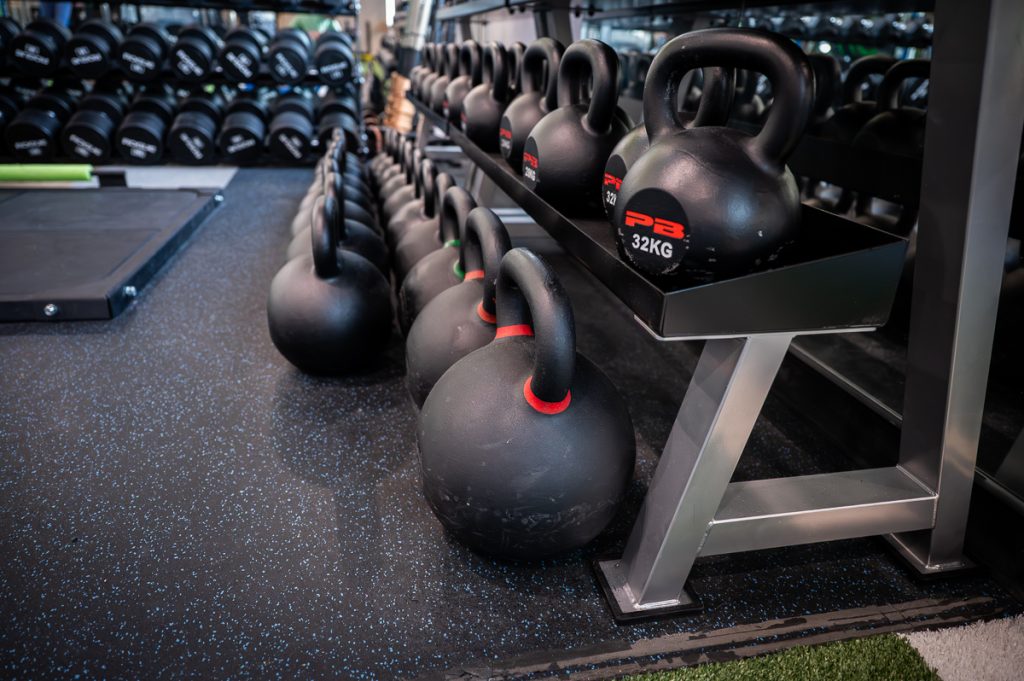 A row of many kettle bells on racks in the perfomance lab.