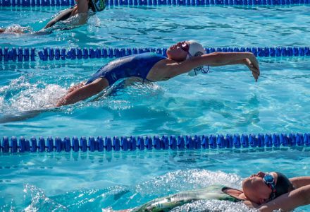 Young swimmers launch from the starting blocks backwards in a backstroke race.
