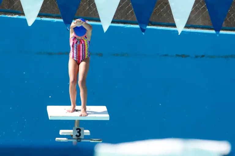 Young swimmer standing on the starting block over the pool