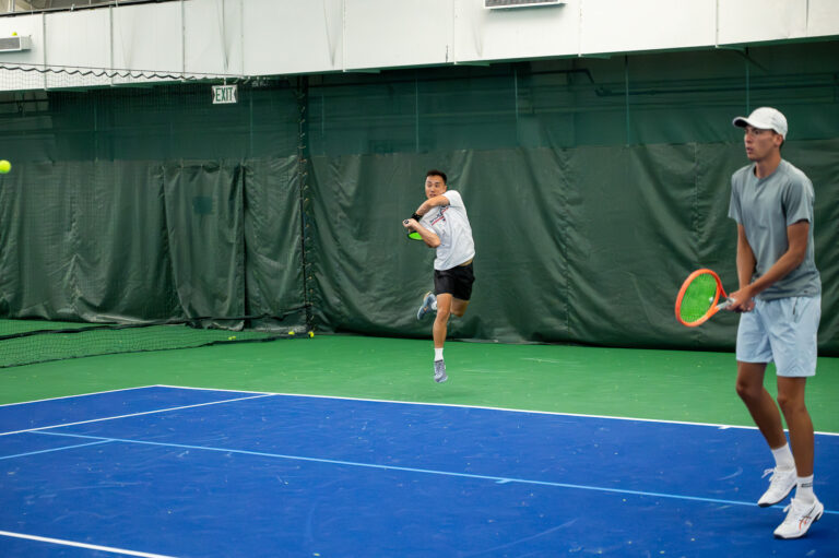 Tennis coach and player rallying on an indoor court