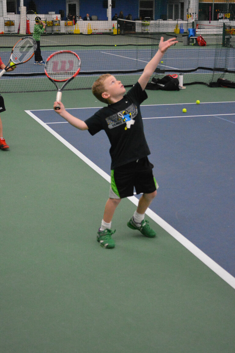 Young boy hitting an overhead in a junior tennis class